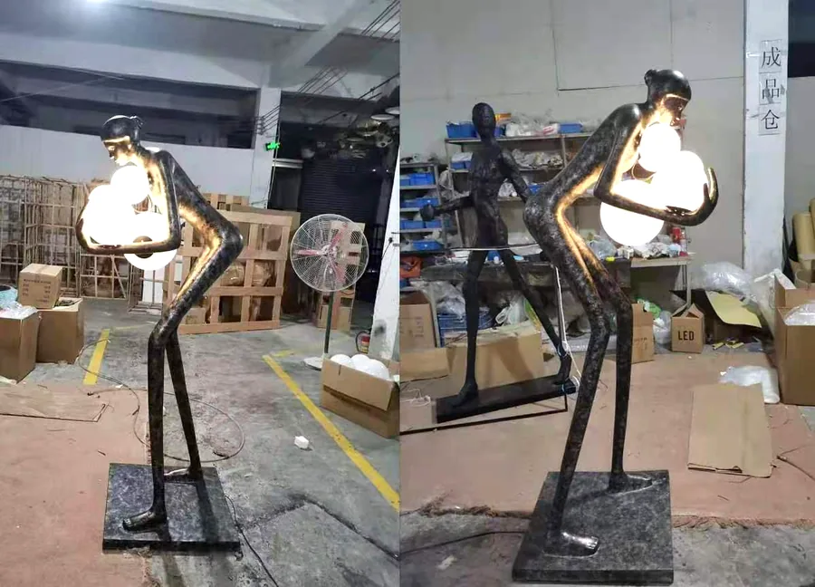 Bronze figure sculpture floor lamps holding glowing glass orbs &mdash; a pair on the factory floor