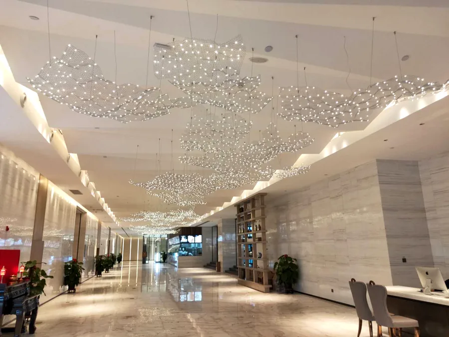 Hotel lobby &mdash; hand-woven mesh cloud light canopy installed above the marble floor