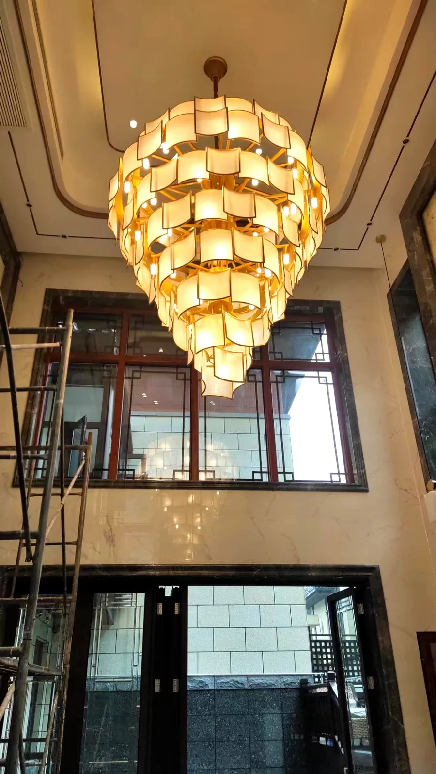 Double-height villa foyer &mdash; silk and copper tiered chandelier during installation